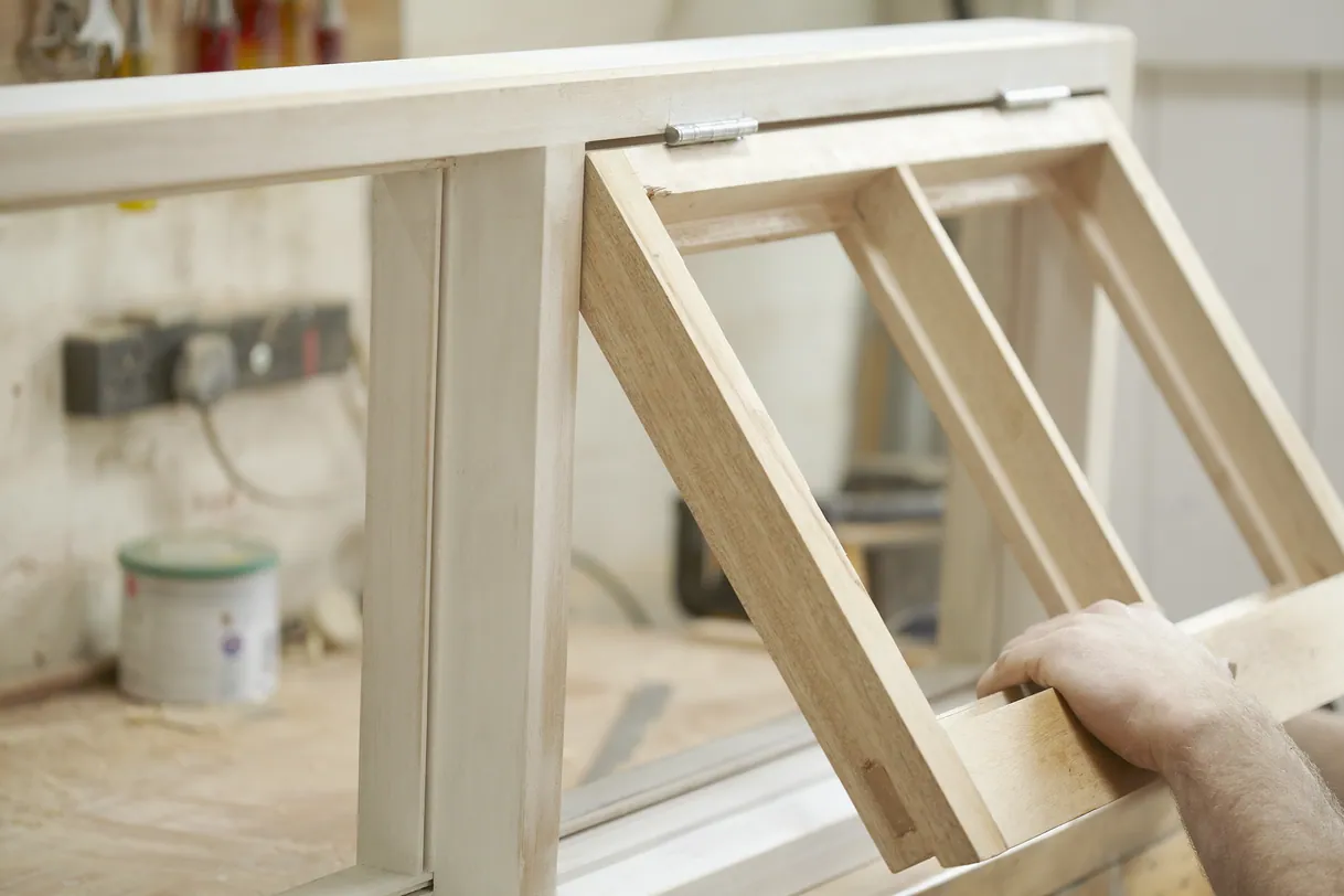 Artisan installant un châssis de fenêtre en bois clair dans un atelier.