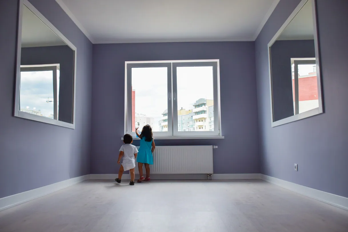 Deux enfants regardent par la fenêtre dans une pièce.