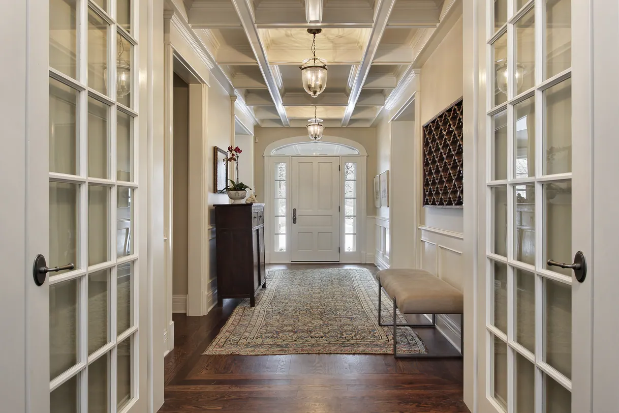 Élégant hall d'entrée avec portes françaises, plafond à caissons, tapis, porte principale.