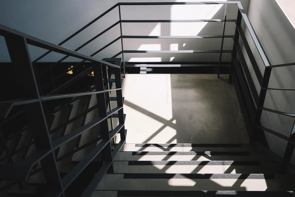 Escalier moderne avec GARDE CORPS en métal, lumière et ombres architecturales fortes.