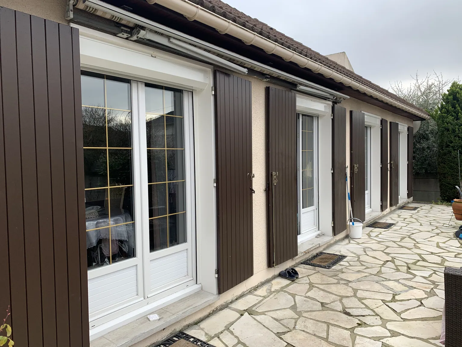 Extérieur de maison résidentielle avec volets marron et fenêtres blanches sur patio.