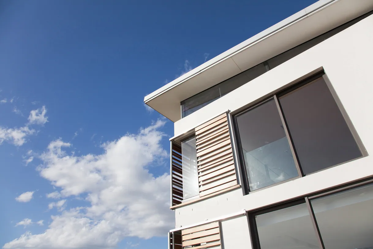Façade bâtiment moderne, fenêtres avec persiennes bois sous ciel bleu.