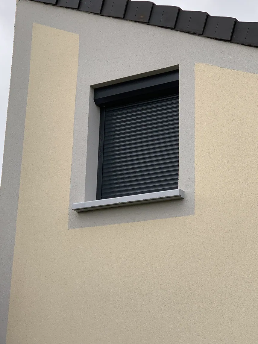 Façade de maison beige avec fenêtre et volet roulant gris fermé