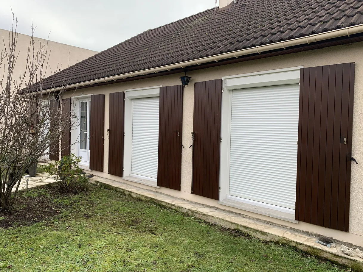 Façade de maison avec volets marron fermés sur fenêtres blanches.