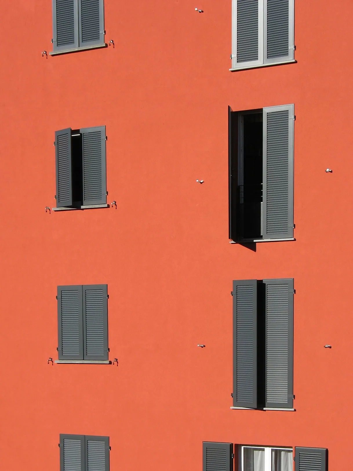 Façade orange d'un bâtiment, fenêtres avec volets gris ouverts et fermés.