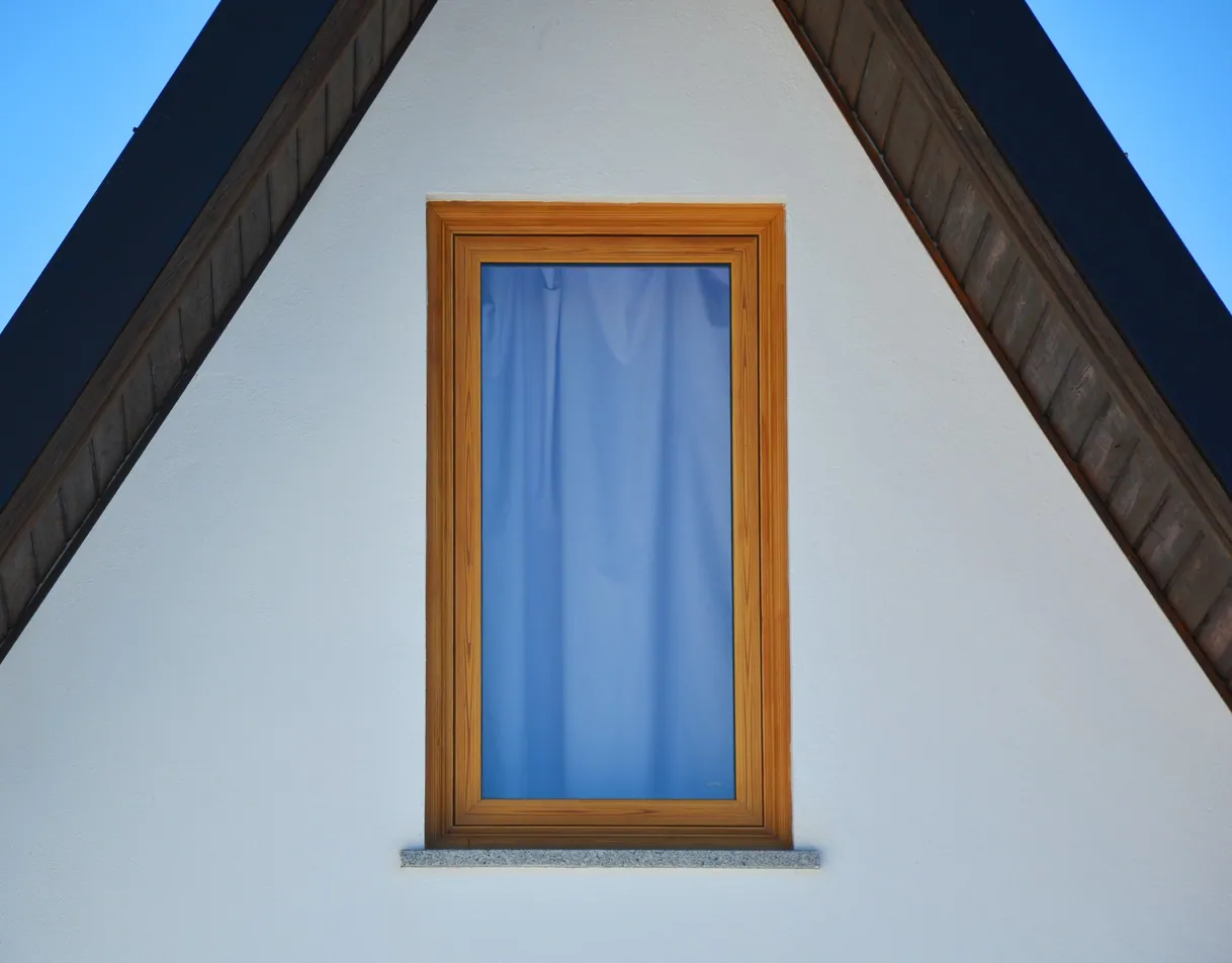 Fenêtre en bois sur mur de grenier blanc avec toit sombre.
