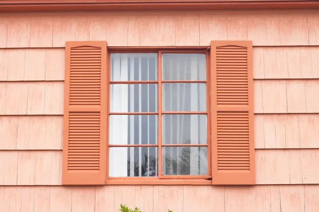 Fenêtre encadrée couleur corail sur mur de maison à bardeaux pêche.