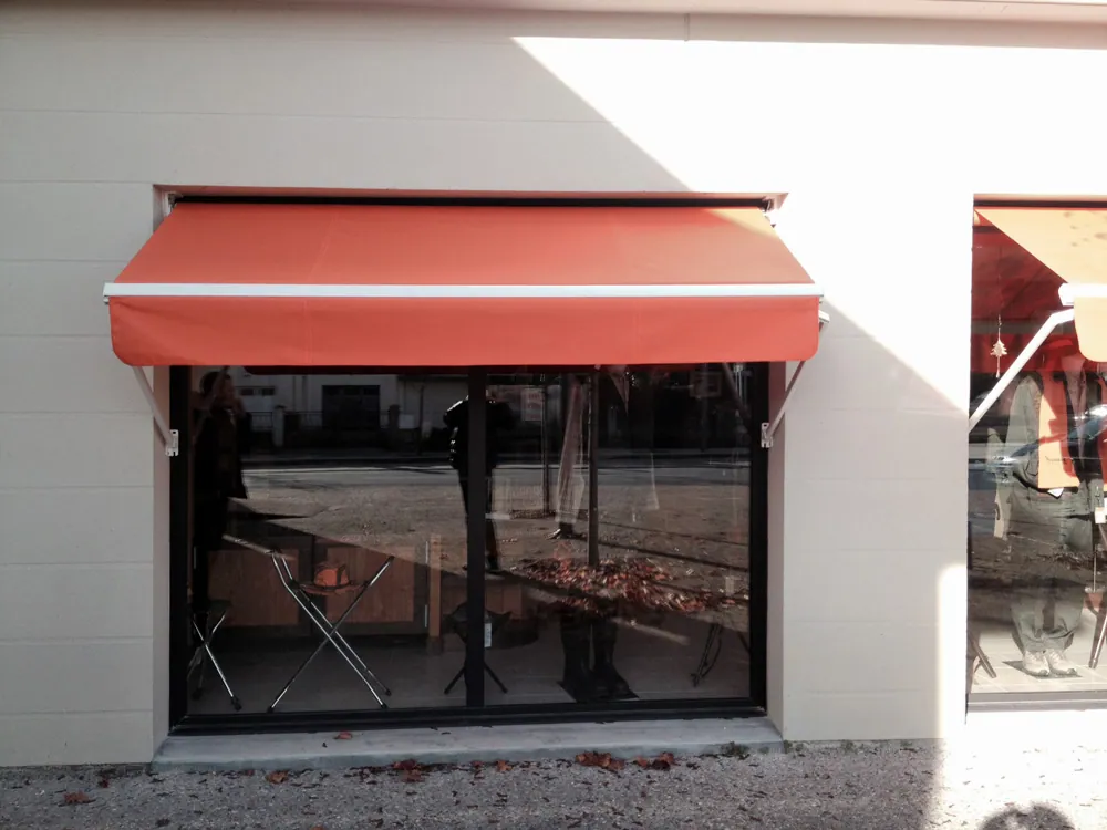 Fenêtre de magasin avec auvent rouge sur façade blanche ensoleillée.