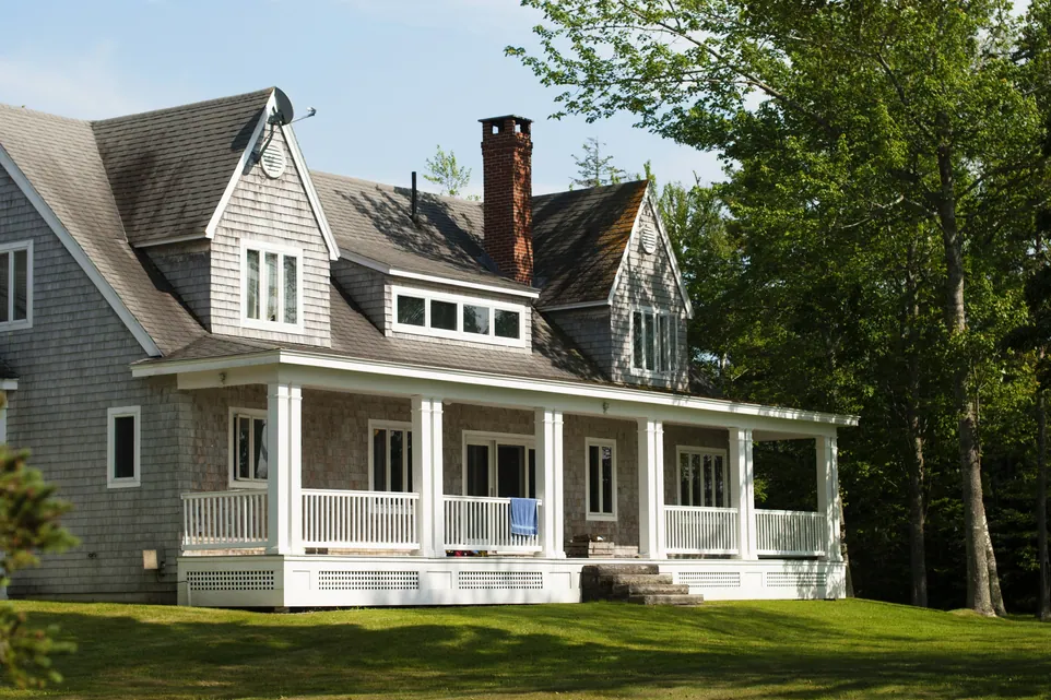 Grande maison grise avec porche blanc, pelouse verte et arbres.