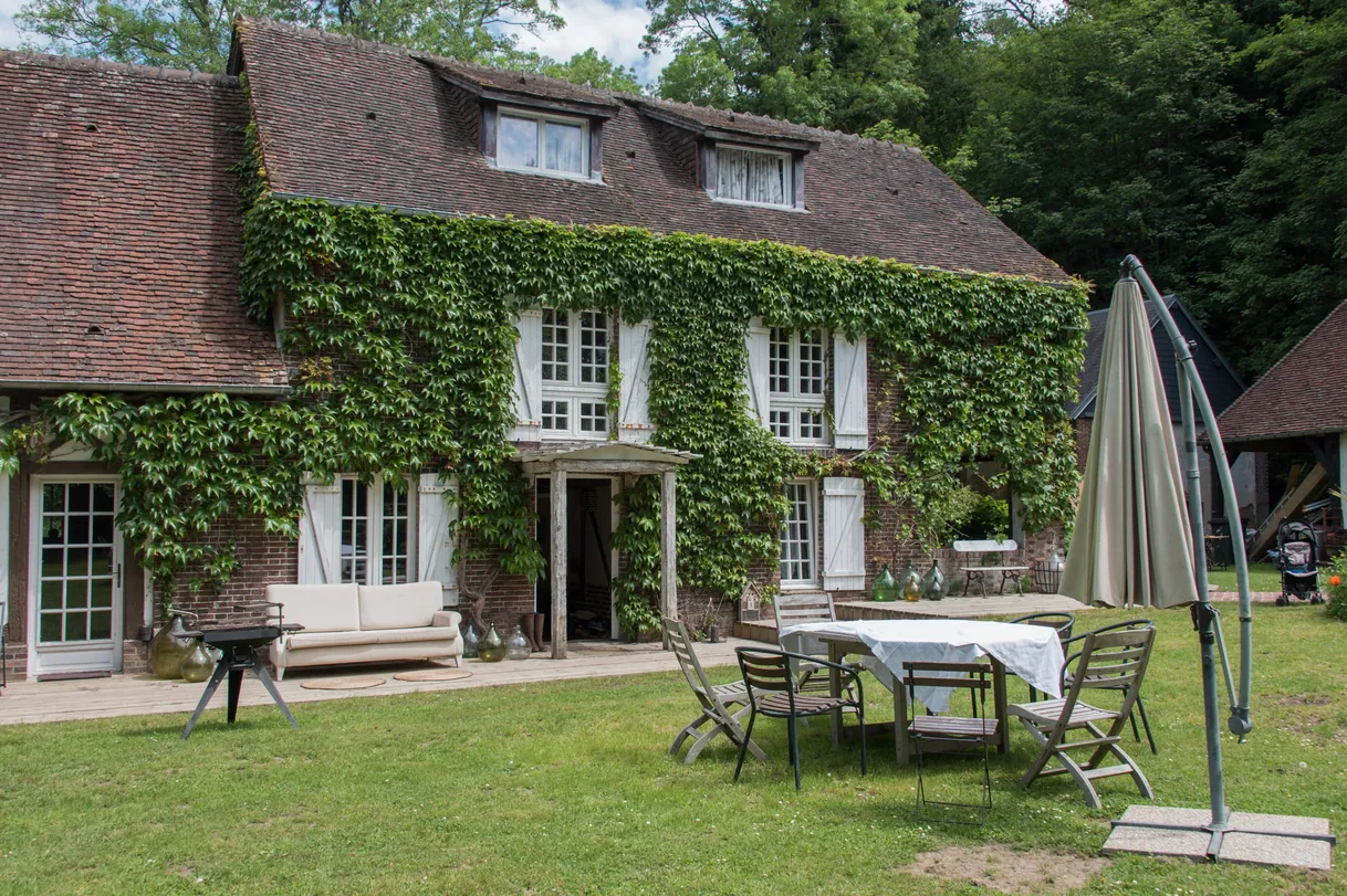 Maison française traditionnelle couverte de lierre luxuriant avec jardin et mobilier d'extérieur.