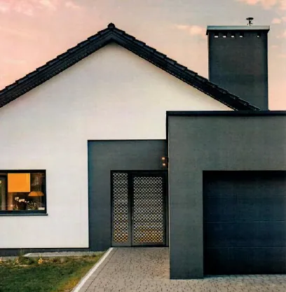 Maison moderne blanche et grise, allée pavée, ciel coucher de soleil orangé.