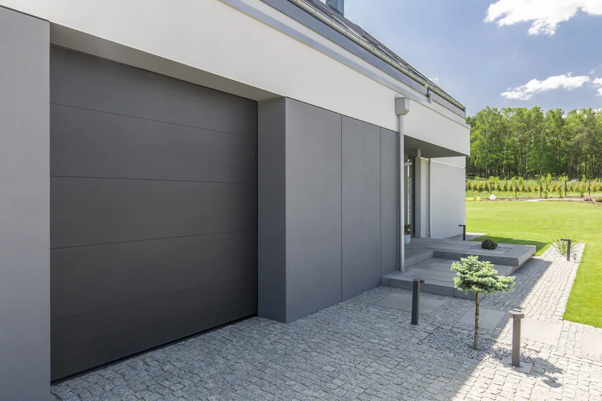 Maison moderne avec porte de garage grise, design minimaliste et pelouse.