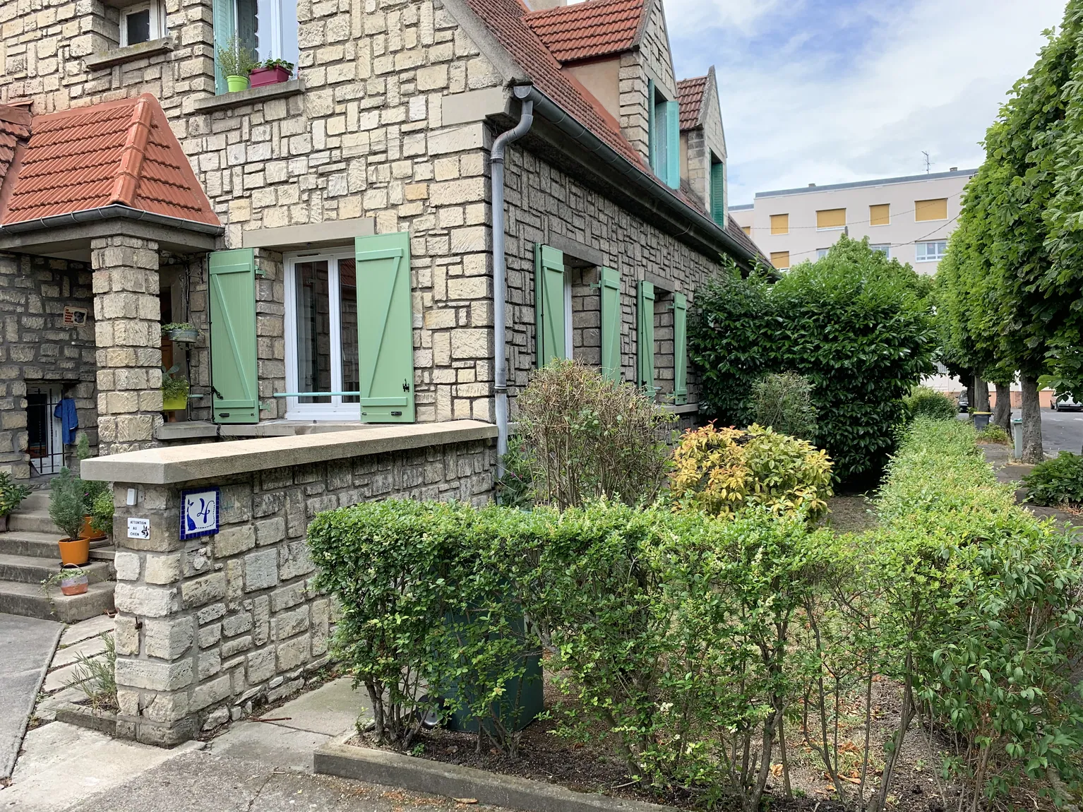 Maison en pierre avec volets verts, toit et jardin bien entretenu.