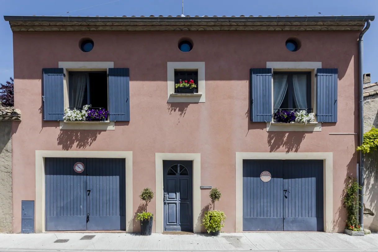 Maison rose avec volets bleus et deux portes de garage.