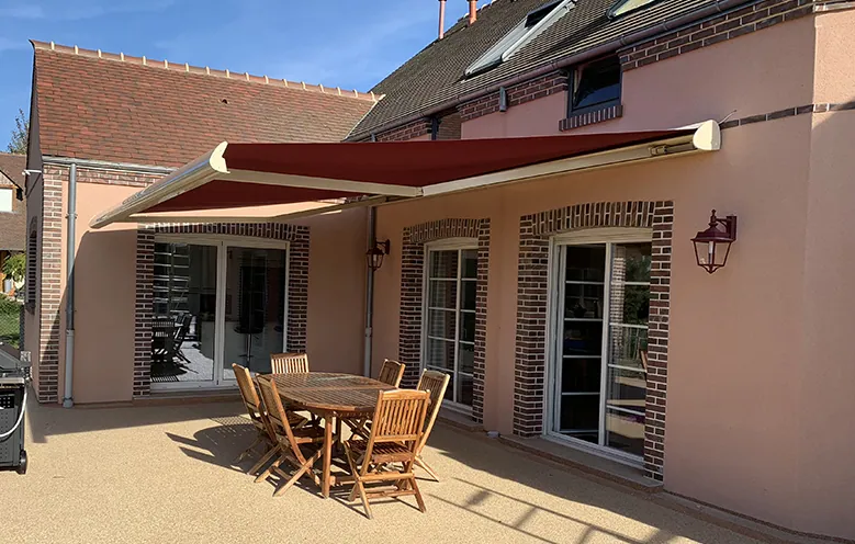 Maison avec terrasse, mobilier de jardin et store banne rouge déployé.