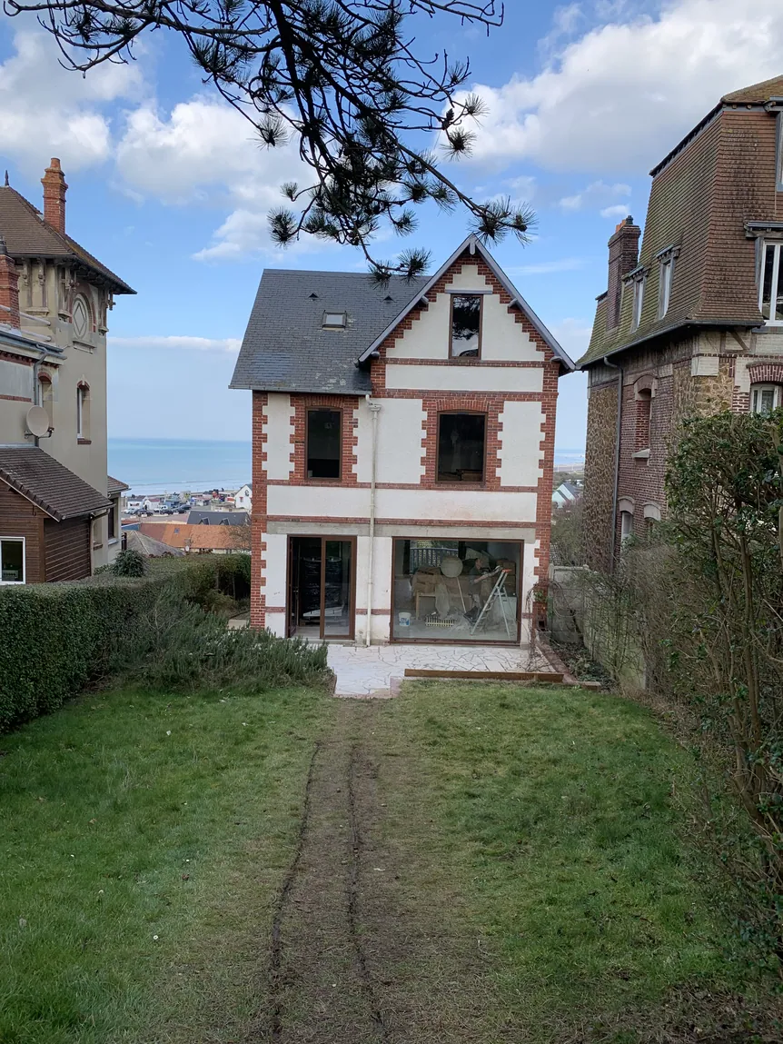 Maison traditionnelle charmante avec façade blanche, chemin herbeux, sous ciel bleu.