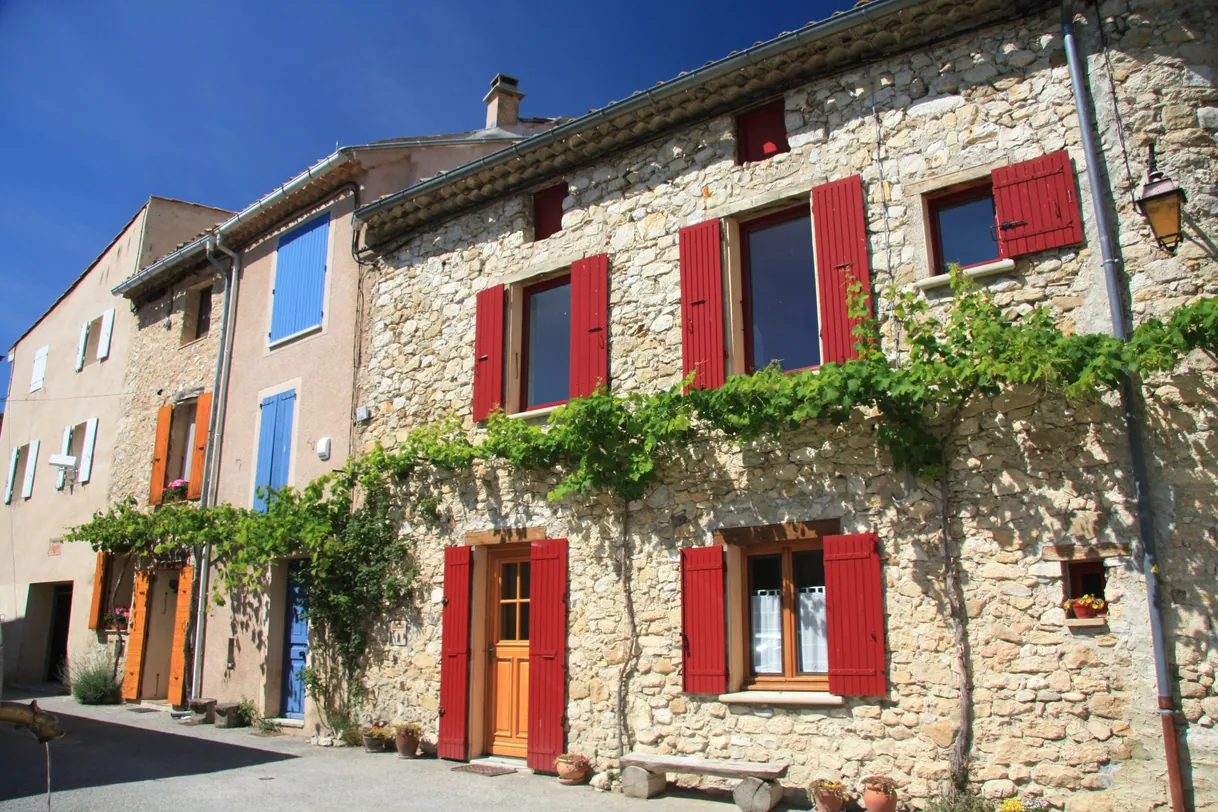Maisons en pierre provençales, volets rouges et bleus, sous un soleil éclatant.