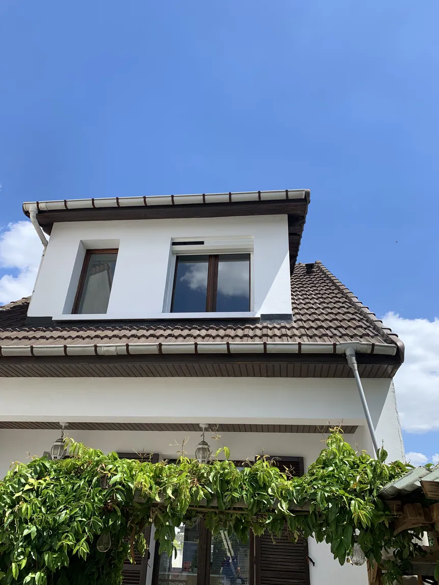 Partie supérieure d'une maison avec toit tuile et lucarne, ciel ensoleillé.