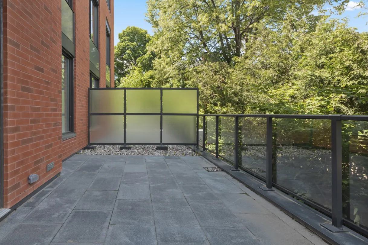 Patio carrelé moderne avec garde-corps en verre et écran de confidentialité.