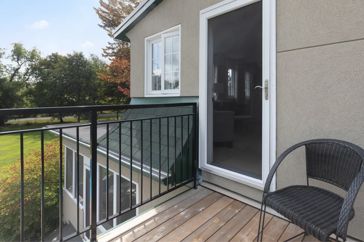 Petit balcon en bois avec chaise noire et porte vitrée, vue verdoyante.