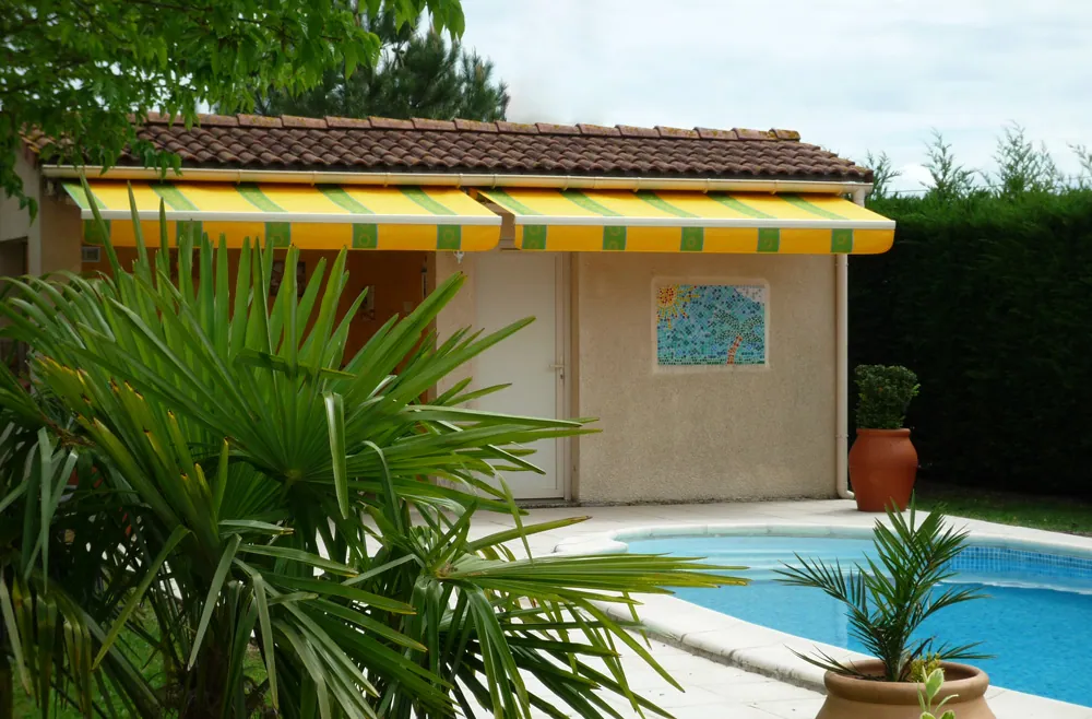 Petit bâtiment de piscine avec auvent jaune et vert près d'une piscine.