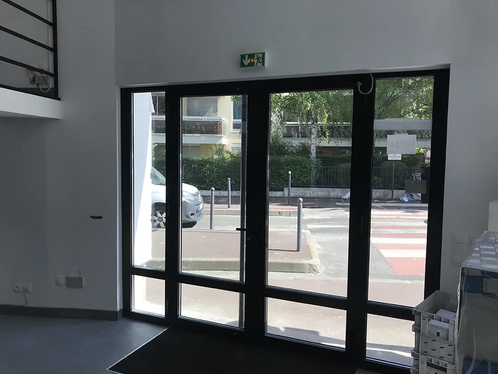 Portes vitrées d'entrée avec panneau de sortie vert, vues sur rue et voiture.
