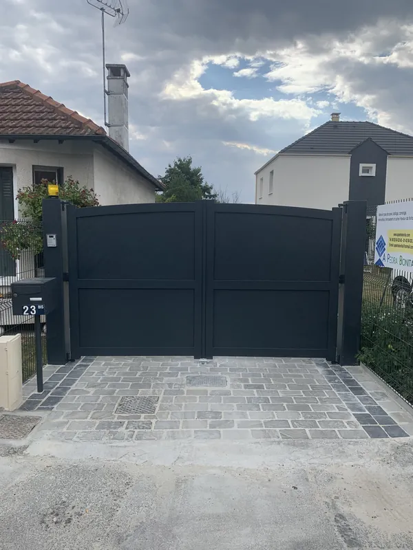 Grand portail coulissant gris foncé pour entrée de maison pavée.