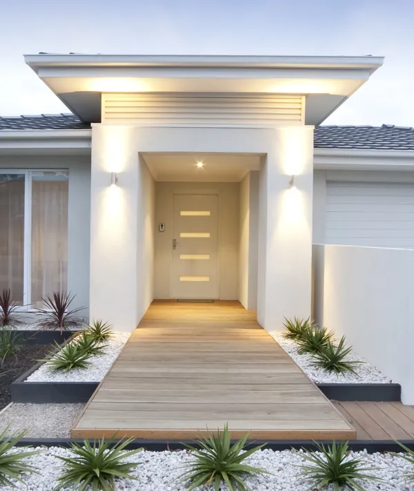 Entrée moderne de maison avec porte blanche, allée bois éclairée, jardins.