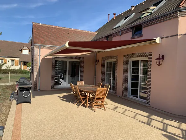 Maison rose, grand patio avec store banne rouge et mobilier extérieur.