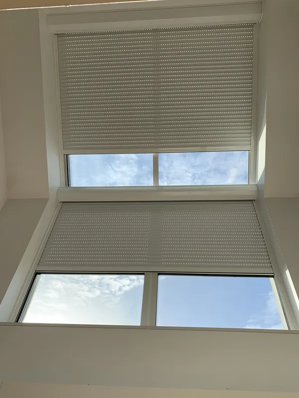 Deux fenêtres de toit avec stores, laissant apparaître le ciel bleu.