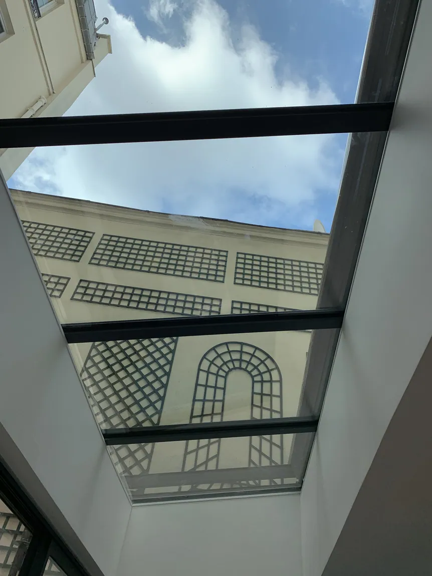 Puits de lumière moderne avec ciel bleu et nuages, reflétant un bâtiment.