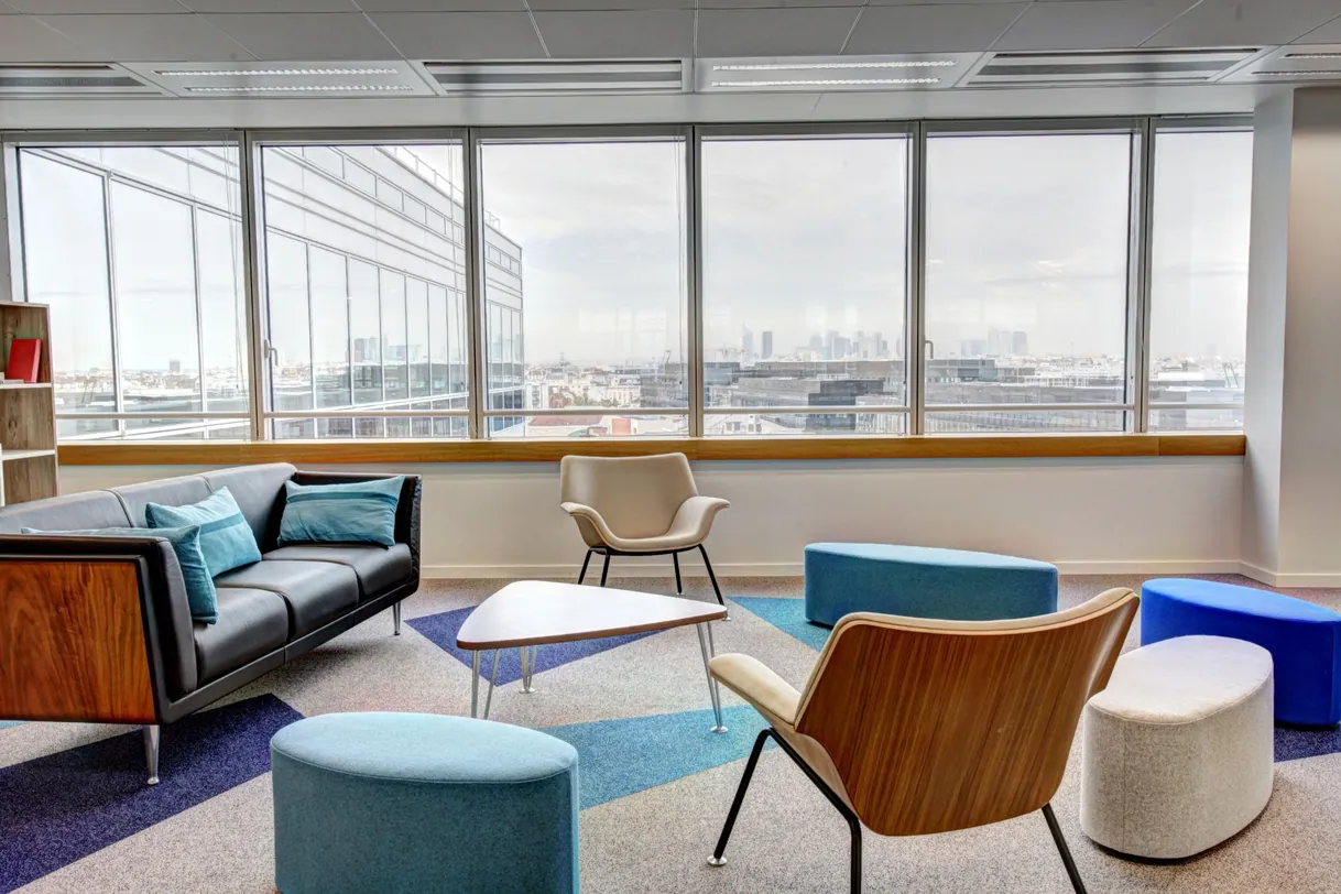 Salon moderne avec canapé, fauteuils et table basse, vue sur ville.