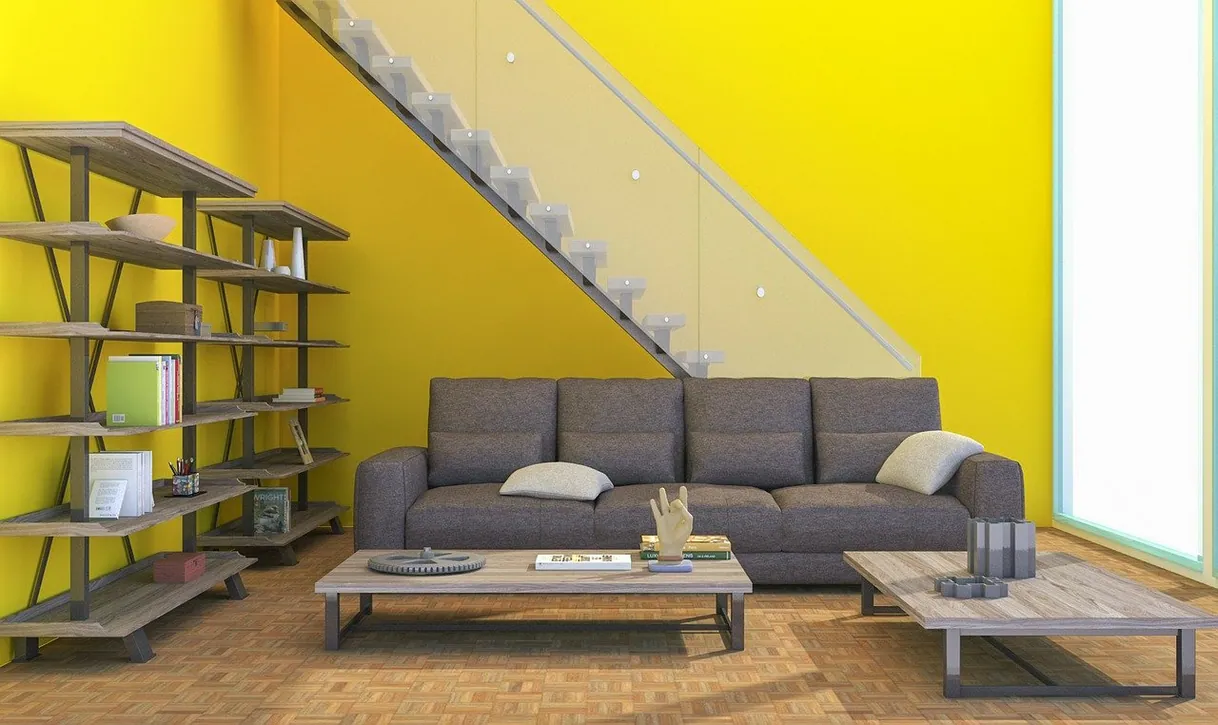 Salon moderne avec canapé gris, tables basses, étagères et mur jaune.