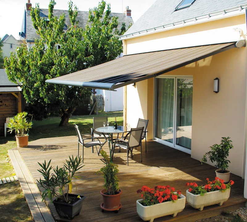 Store banne gris étendu protégeant une terrasse avec mobilier et plantes.