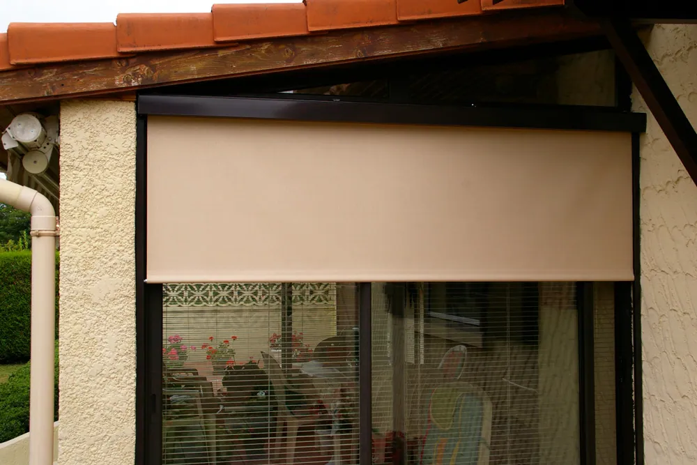 Store enrouleur extérieur beige installé au-dessus d'une fenêtre de maison.