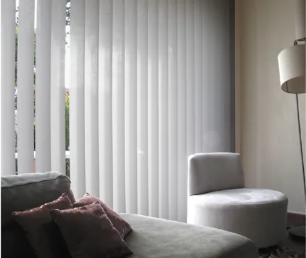 Stores verticaux blancs pour fenêtre avec canapé et lampe.