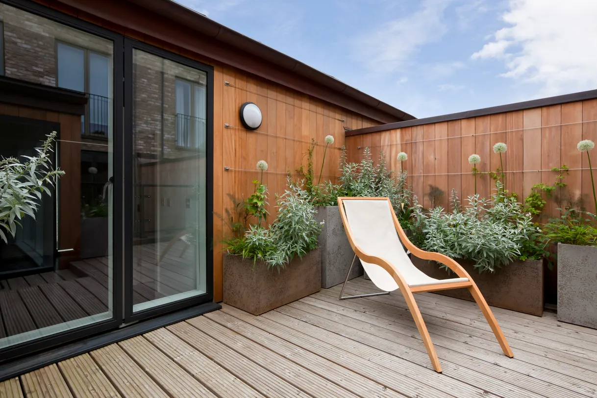 Terrasse chic sur le toit avec transat en bois et plantes vertes.