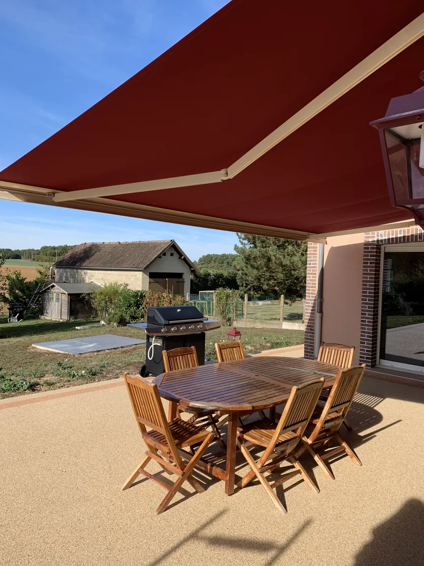 Terrasse extérieure avec auvent rouge, table en bois et barbecue.