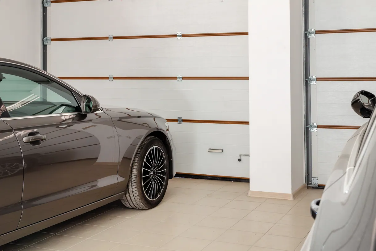 Voiture marron garée dans un garage moderne avec portes sectionnelles blanches.